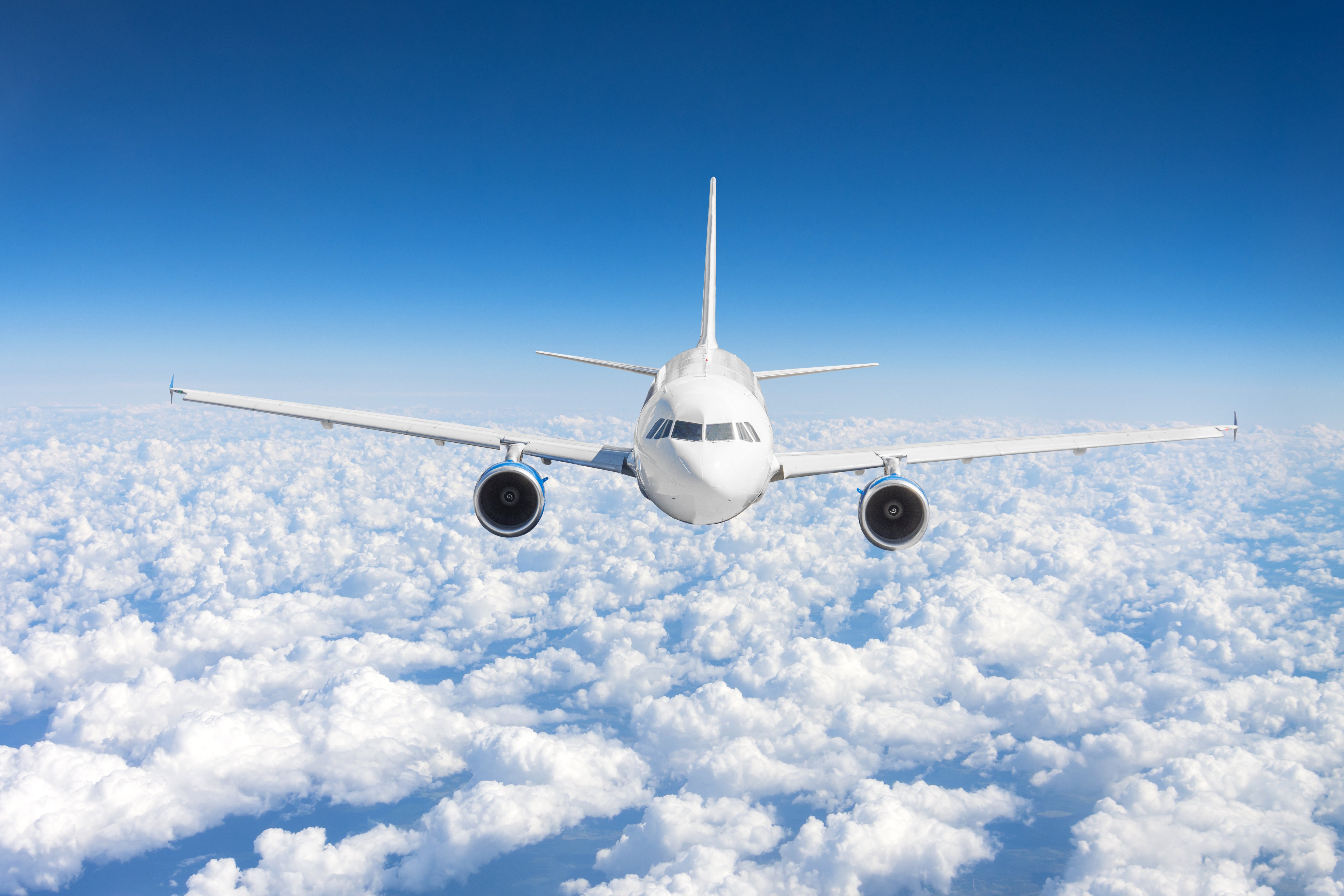 Airplane jet flying at flight level high in the sky above the clouds and blue sky.